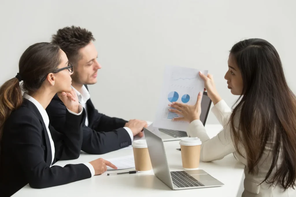 Equipe em reunião analisando gráficos em um documento e discutindo relatórios no escritório, enquanto a cliente explica dados; imagem sobre como a experiência do cliente impacta os resultados da empresa.