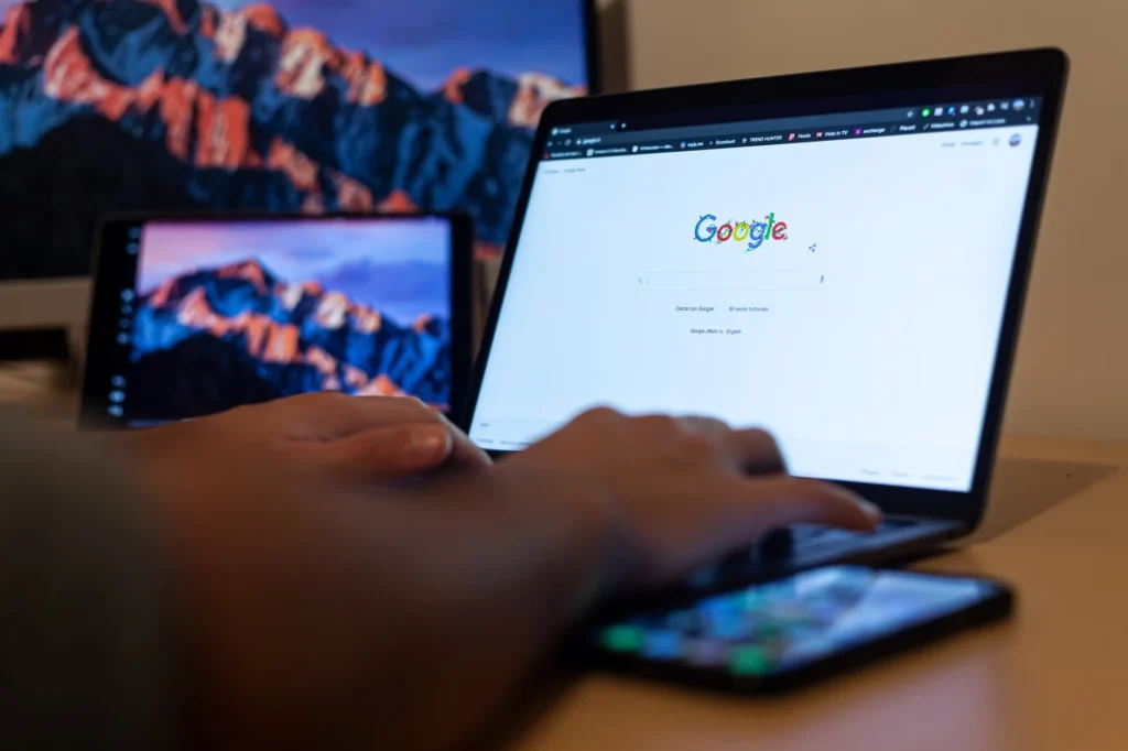 Pessoa usando notebook com página do Google aberta, com outro monitor ao fundo, em ambiente de trabalho; ideia de como empresas em Curitiba podem usar Google Ads para vender mais.